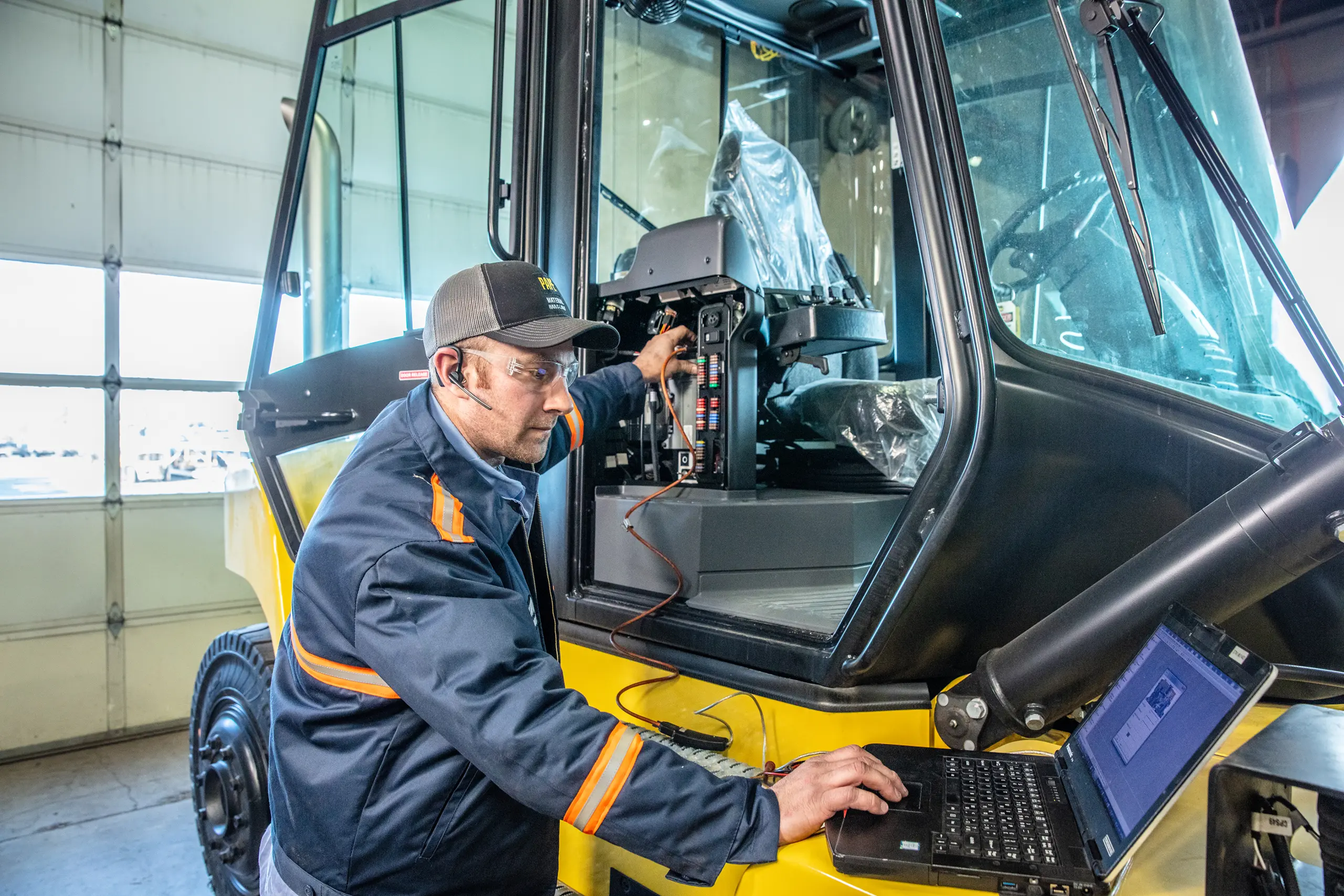 Technician diagnosing forklift wiring with laptop