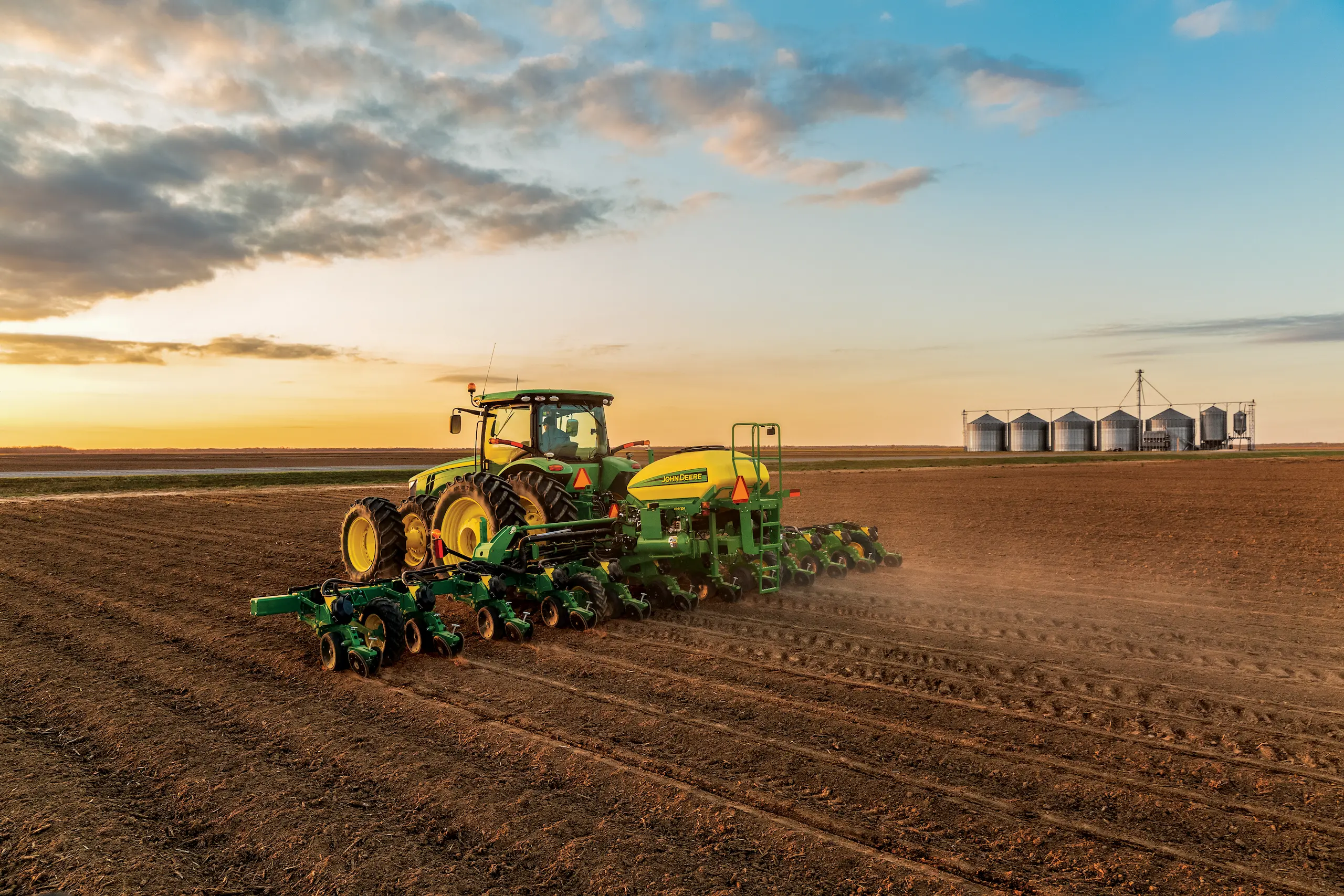 Tractor planting field near grain silos