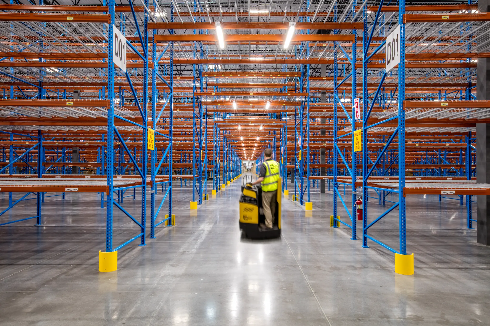 Worker riding cart through empty warehouse aisle