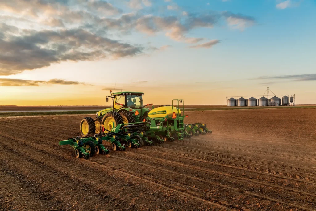 Tractor planting field near grain silos