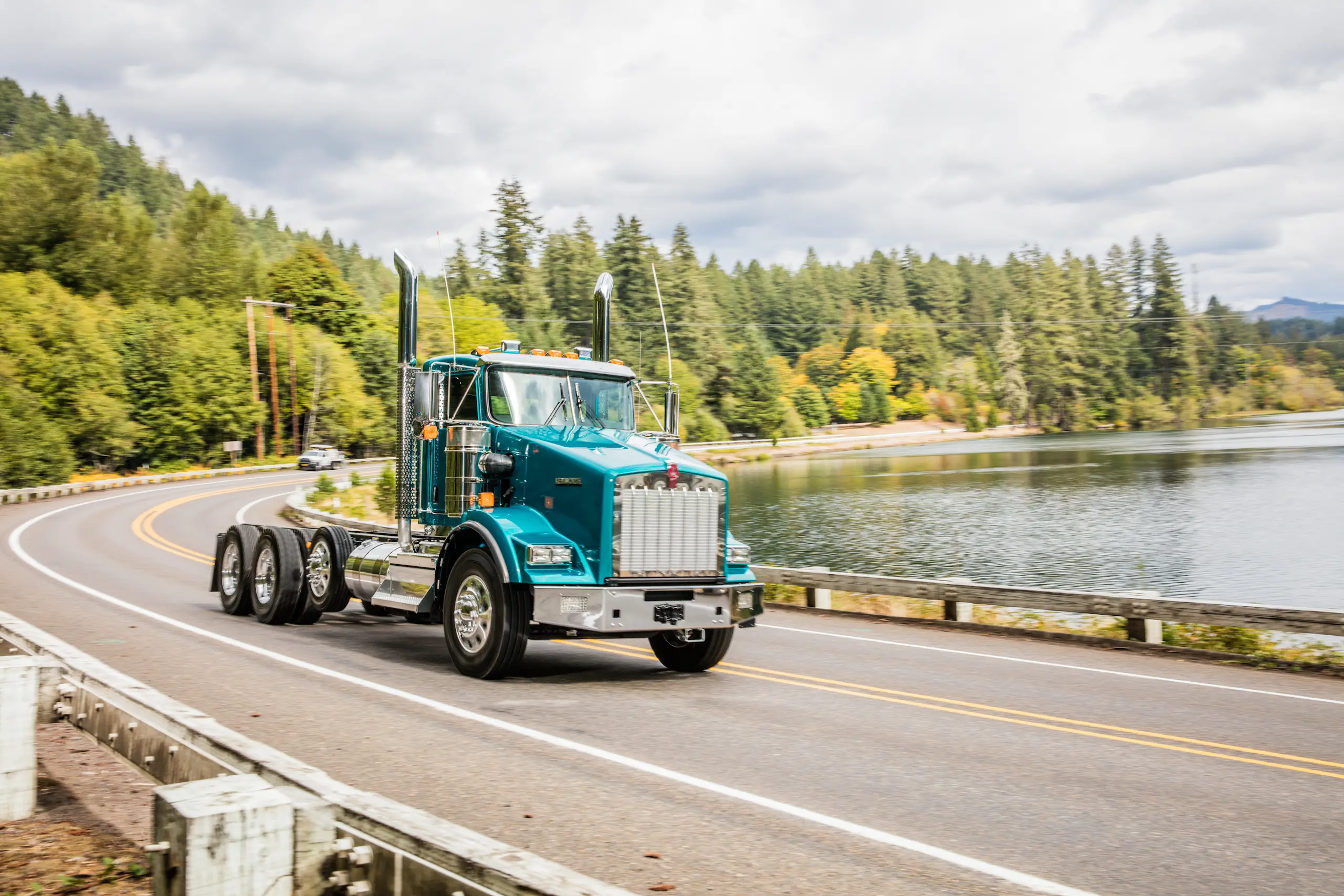 Teal Kenworth truck driving lakeside road
