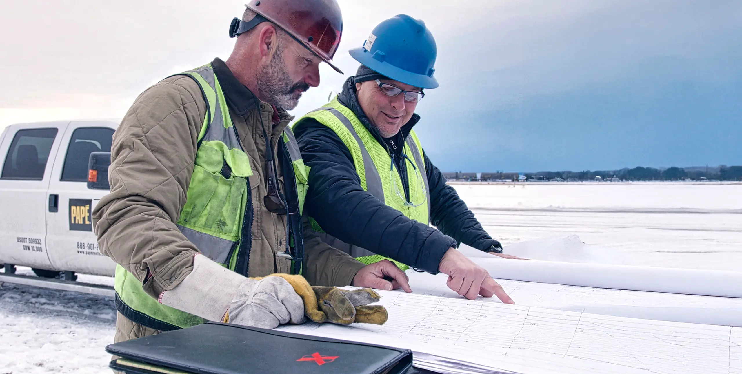 Workers reviewing blueprints in snowy site