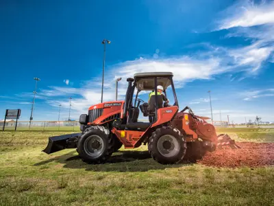 Red tractor tilling grass near field