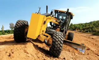 Yellow motor grader smoothing dirt road