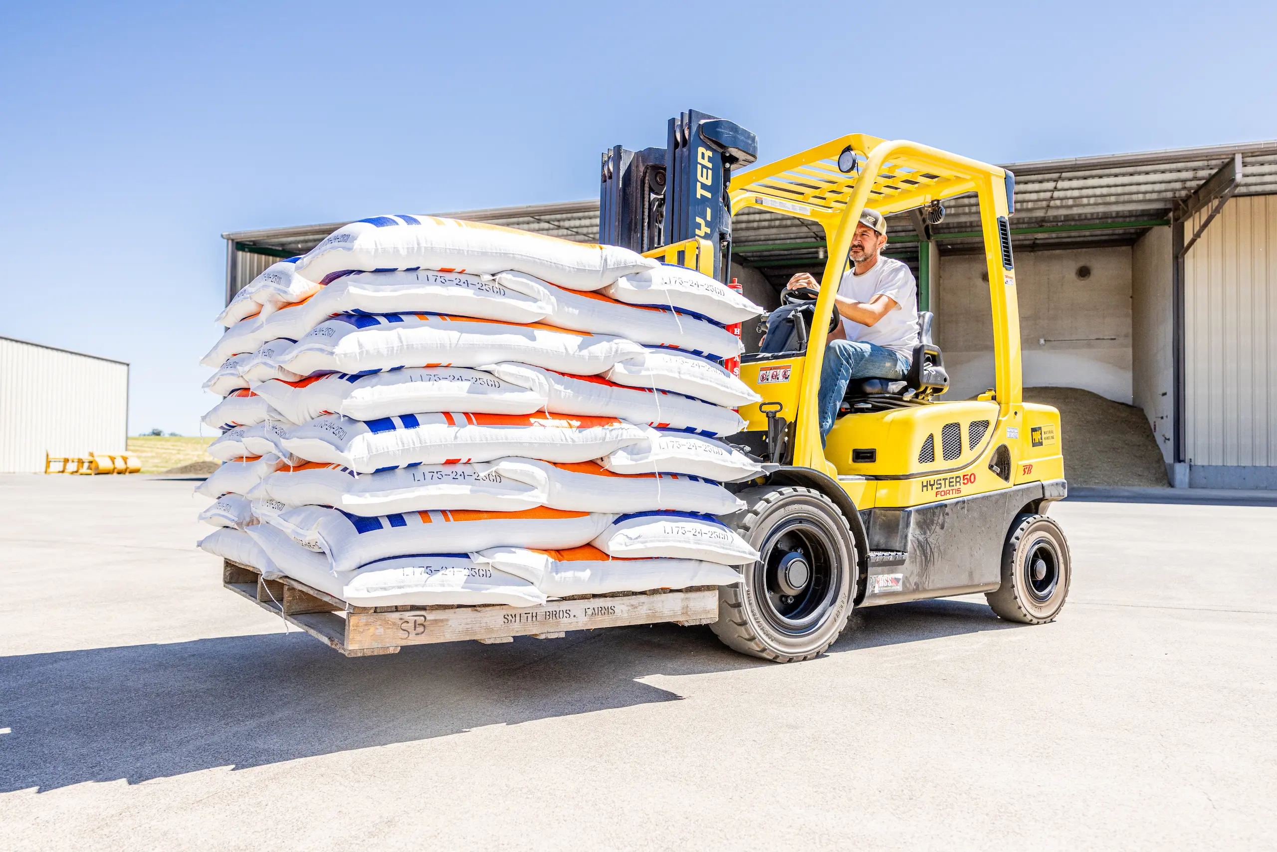 Forklift transporting stacked feed bags outside