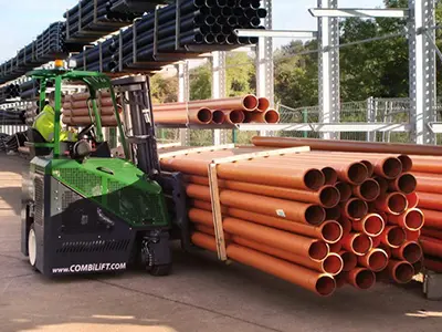 Green forklift moving stacked orange pipes